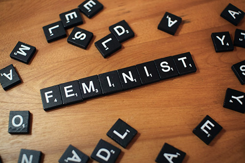 Feminist spelled on word tilesjpg Black and white Scrabble wood letter blocks form the word FEMINIST on a wooden table top
