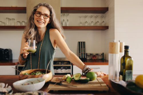 Healthy senior woman smiling while holding some green juice in her kitchen. Mature woman serving herself wholesome vegan food at home. Happy woman taking care of her aging body.