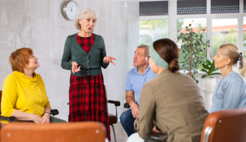 Friendly aged woman conducting language speaking club, communicating with group of interested older adults