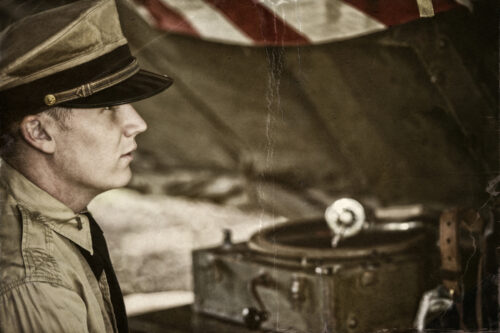 Aged Photo of Naval officer enjoying some down time in his tent listening to his photograph play records. Grain and cracking from aging process... NOTE: These are authentic, professional WWII reenactment actors and models wearing authentic WWII era US Army military uniforms and