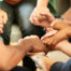 Close-up of a group of diverse people sitting in a circle and holding hands together during a support group meeting