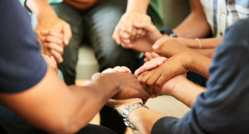 People holding hands together during a support group meeting Close-up of a group of diverse people sitting in a circle and holding hands together during a support group meeting