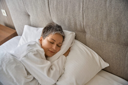 Adult lady in white bathrobe resting in hotel room while sleeping on cozy pillow.