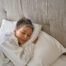 Adult lady in white bathrobe resting in hotel room while sleeping on cozy pillow.