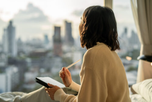 Asian woman writing her to-do list on digital tablet, writing down her goals, determined to stay motivated and on track to accomplish new things in the New Year