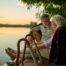 Elderly couple is enjoying a peaceful evening on a wooden pier, sharing a blanket and watching the sunset over the lake